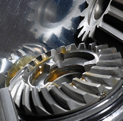 three gears connecting with drops of oil against shiny steel